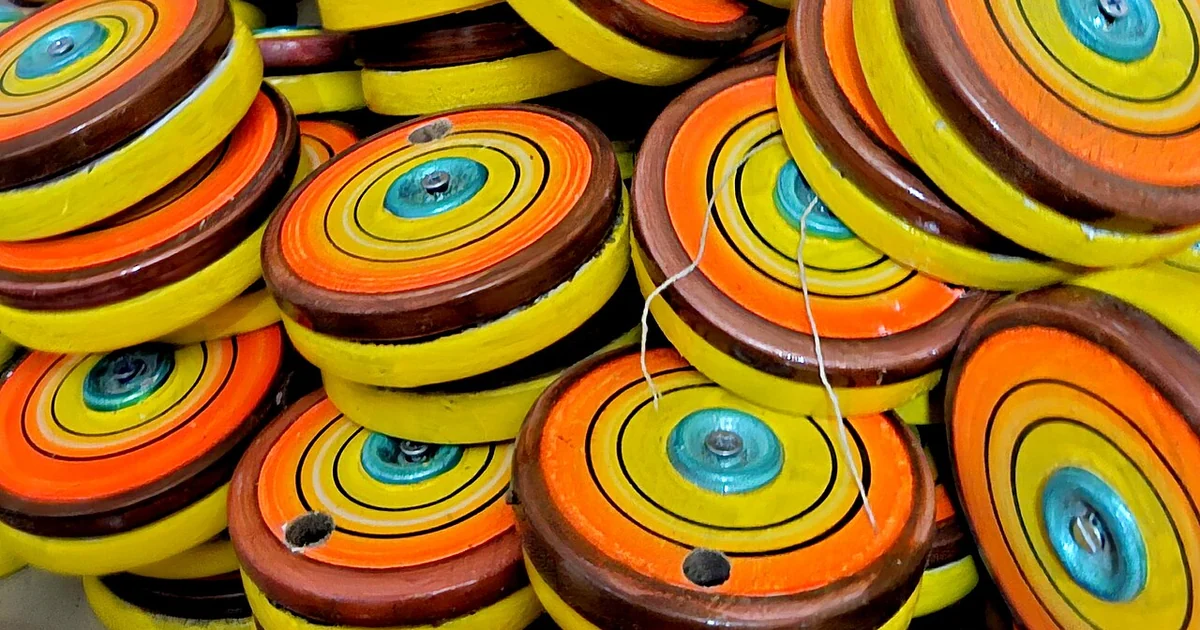 A set of brightly painted wooden toy grinders (chakki) crafted as part of Bhatukali, a traditional miniature household play set, displayed at a workshop in Sawantwadi, Maharashtra, India. These handcrafted models replicate the look of tradi